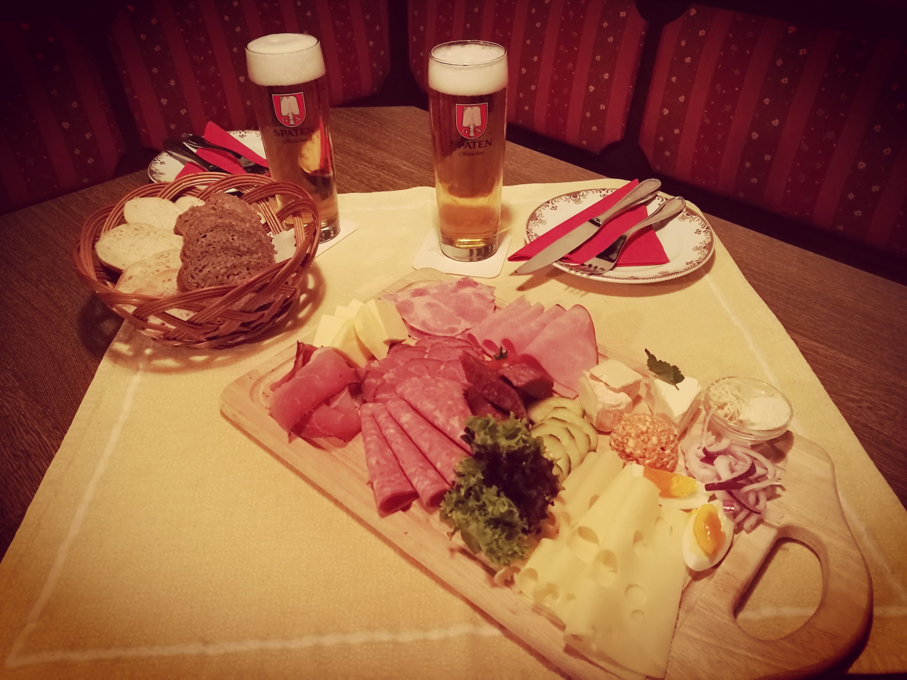A table with a charcuterie board, two glasses of beer, and a basket of bread.