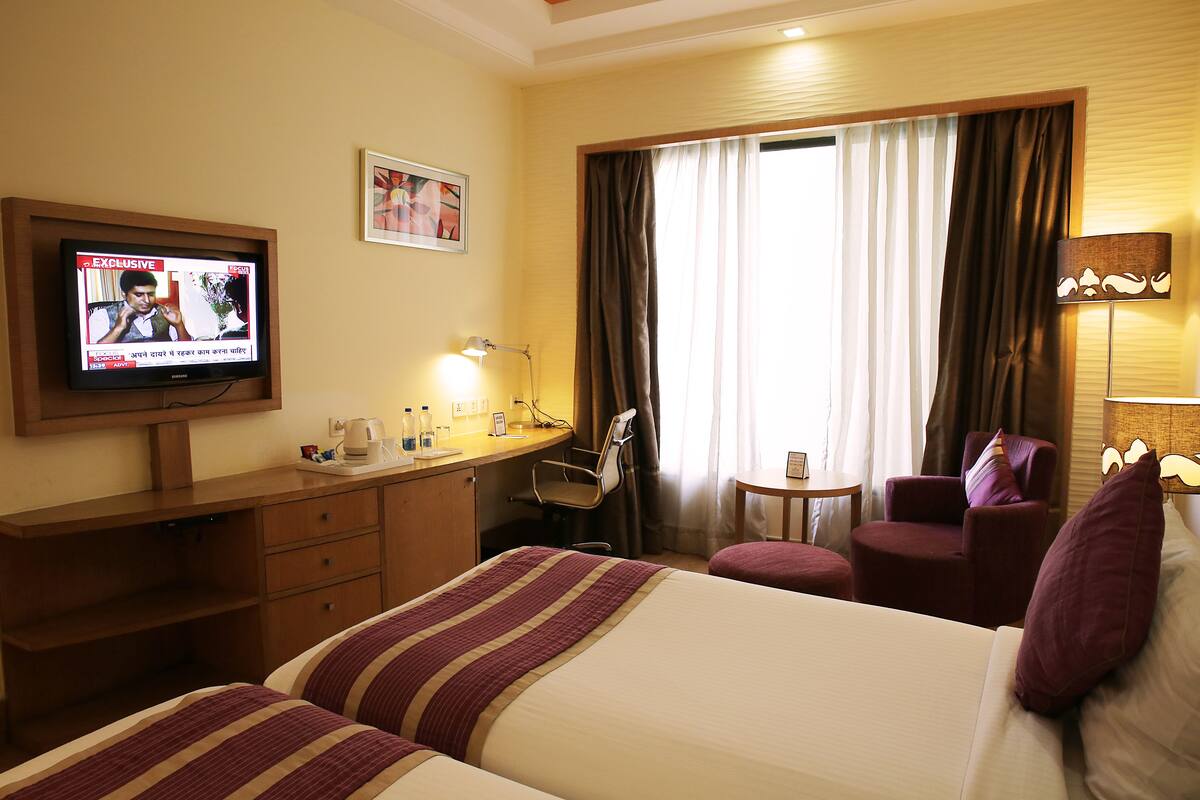 Une chambre d’hôtel équipée d’un lit, d’un bureau, d’une télévision, d’une chaise et d’une fenêtre avec des rideaux.