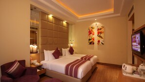 Habitación de hotel con una cama grande, dos mesitas de noche, un televisor y una zona de estar con un sillón y reposapiés.