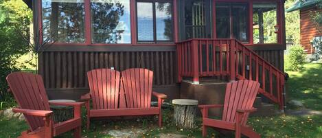 A cabin with a deck, two Adirondack chairs, and a small table.