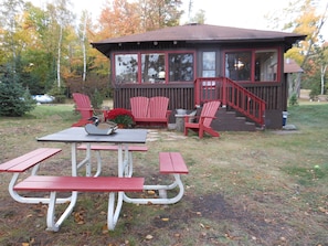 A wooden cabin with a deck, red Adirondack chairs, and picnic tables.