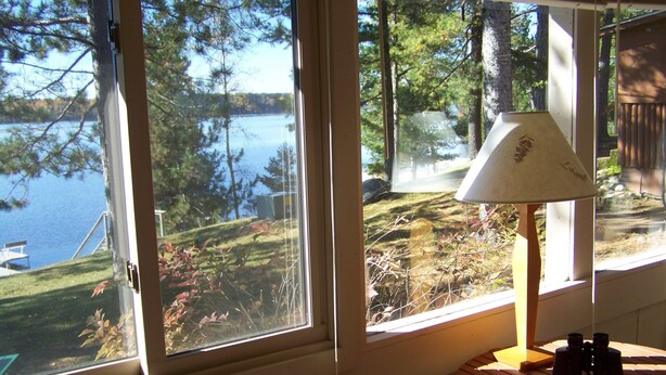 Una habitación con vista a un lago, una lámpara y unos binoculares sobre una mesa.