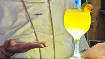 Een persoon in een wit shirt met de tekst 'CHOICE' erop, zittend aan een tafel met een geel drankje in een glas.