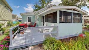 Une petite maison bleu clair avec un porche, un barbecue et des meubles pour s’asseoir à l’extérieur.