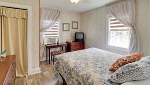 Une chambre à coucher avec un lit, un bureau avec une télévision et une fenêtre avec des rideaux.