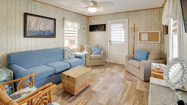 Un salon chaleureux avec un canapé bleu, des fauteuils beiges, une table basse en bois et un ventilateur de plafond.