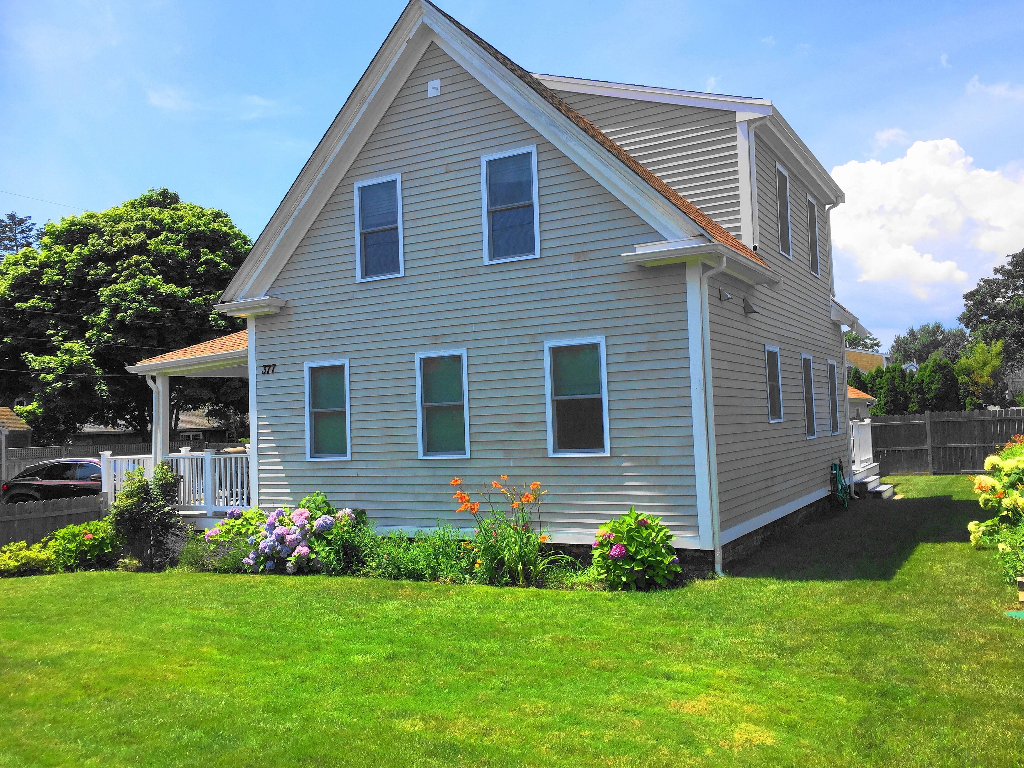 A two-story house with a gabled roof, a covered porch, and a well-maintained front yard with various plants and flowers.