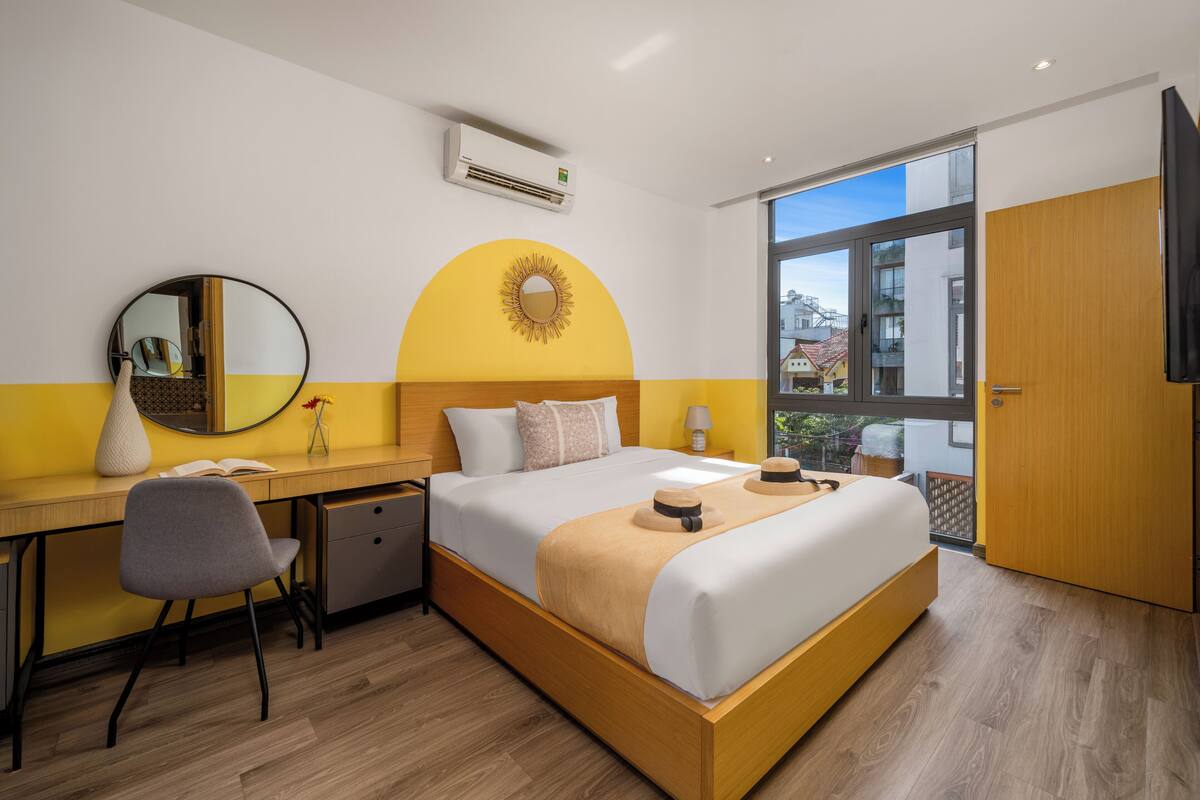 Una habitación de hotel moderna con cama, escritorio, silla y un ventanal grande.