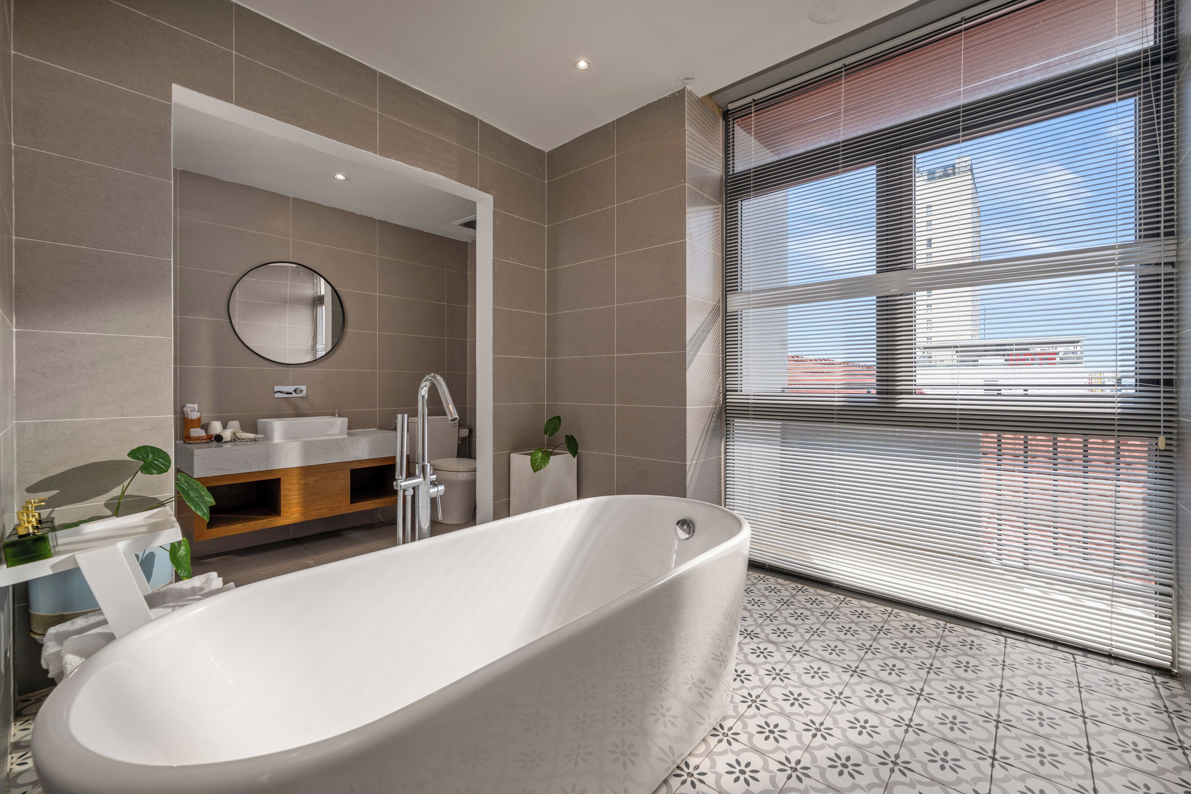 A modern bathroom with a freestanding bathtub, a round mirror, a sink, and a toilet.