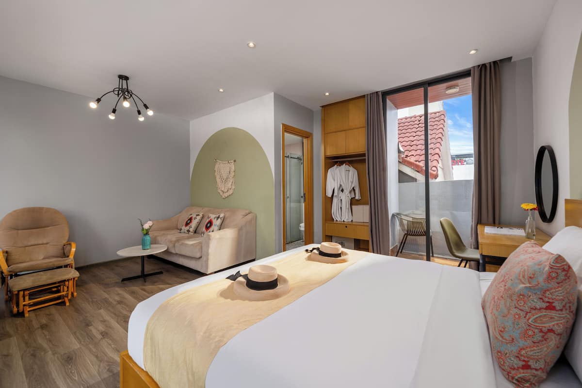 Una habitación de hotel con cama, sofá, sillón, una mesita y armario.