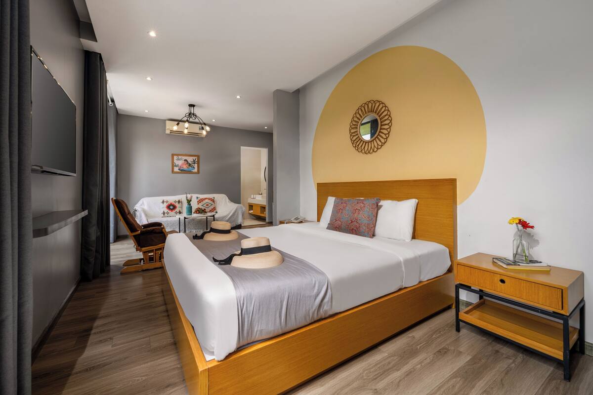 Habitación de hotel moderna con una cama grande, una mesita de noche de madera, una silla y un escritorio con silla.