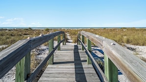 Una pasarela de madera que conduce a la playa, con vista despejada al océano y a las dunas.
