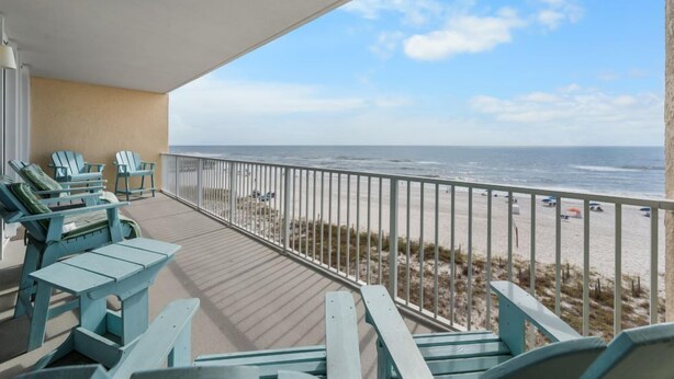Ein Balkon mit Blick auf den Strand, ausgestattet mit einer Holzterrasse und mehreren Adirondack-Stühlen.