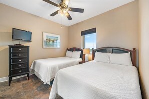 A hotel room with two beds, a TV, a dresser, and a ceiling fan.