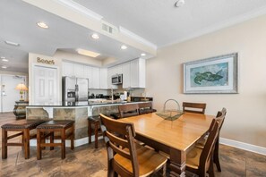 A modern kitchen with white cabinets, a central island, and a dining area with wooden chairs.