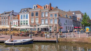 A canal-side restaurant with outdoor seating, a boat docked at the water's edge, and traditional European architecture. - LOT Hotel (Leiden)
