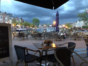An outdoor café with wicker chairs and tables, overlooking a canal with boats and historic buildings in the background. - LOT Hotel (Leiden)
