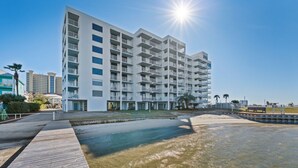 Un hotel moderno de varios pisos con balcones, una zona de piscina y cielo despejado.