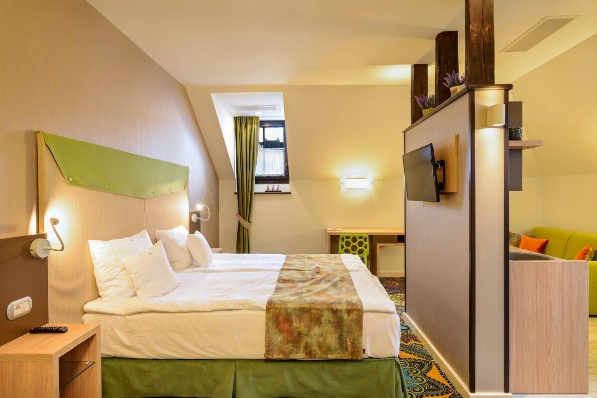 A hotel room with a bed, bedside table, TV, and a small desk with a chair.