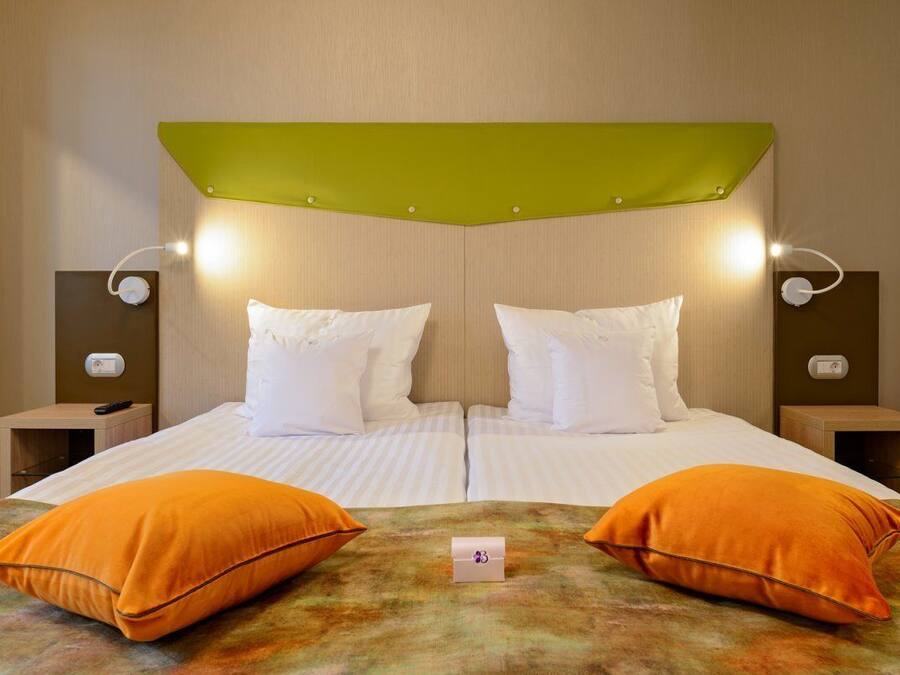 Una cama doble con dos almohadas naranjas, un cabecero verde y lámparas de noche.