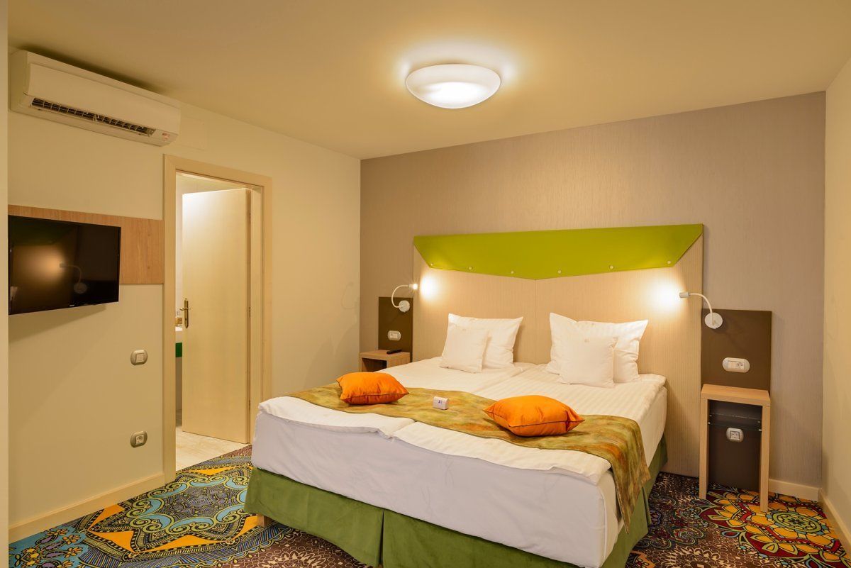 A hotel room with a bed, a television, a green headboard, and a patterned floor.