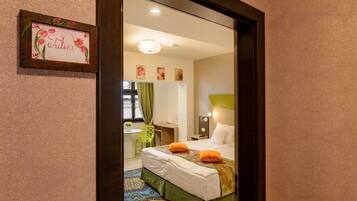 A hotel room with a bed, a desk, a chair, a mirror, and a framed picture on the wall.