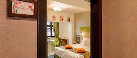 A hotel room with a bed, a desk, a chair, a mirror, and a framed picture on the wall.