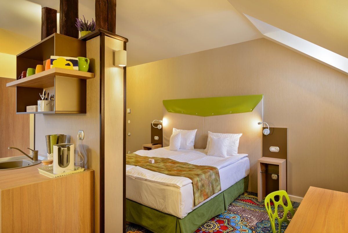 Una habitación de hotel pequeña con una cama, mesitas de noche, un escritorio y una silla.