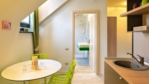 A modern kitchen with a round table, green chairs, a built-in sink, and a view into the adjacent bathroom. - Blumenhaus Sibiu (Sibiu)