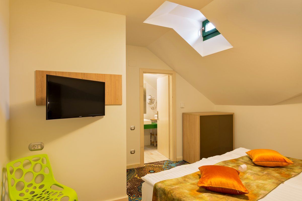 Een hotelkamer met een bed, een aan de muur bevestigde televisie, een groene stoel en een dakraam.