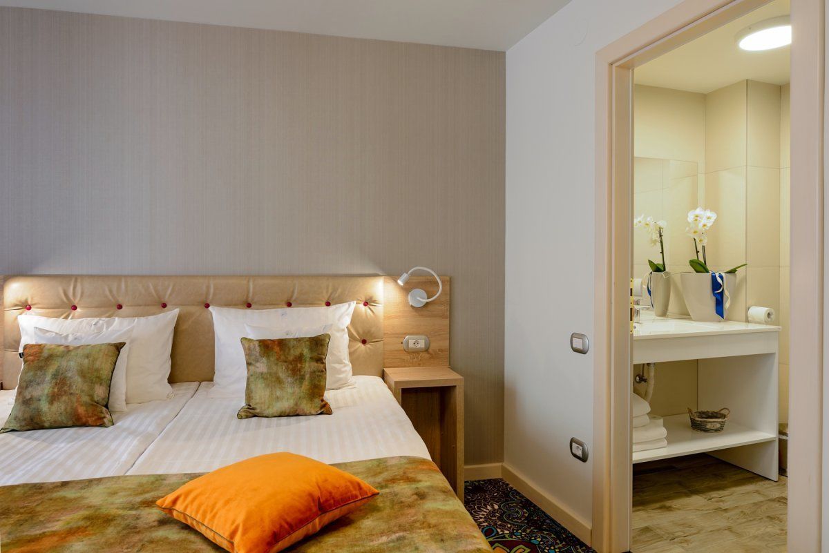 A neatly arranged hotel room with a bed, bedside tables, and a bathroom visible through an open door.