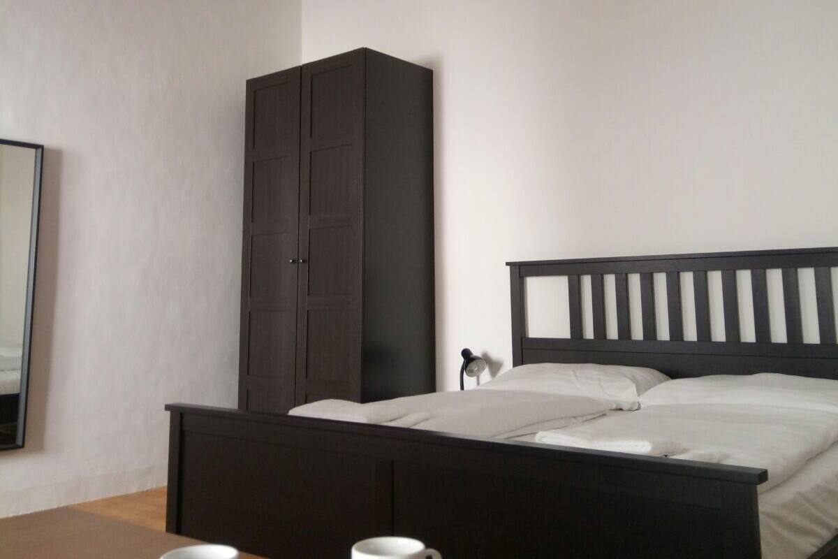 A bedroom with a bed, a wardrobe, a table with two cups, and a chandelier.