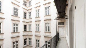 A multi-story building with a white facade, a balcony with a black railing, and a door at the end of the corridor. - City Center Homes (Vienna)