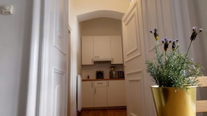 A narrow hallway leading to a kitchen with white cabinets and a wooden floor. - City Center Homes (Vienna)