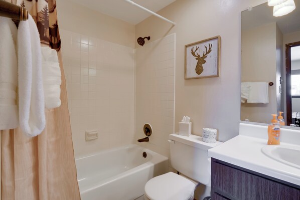 Un baño con bañera, inodoro y lavamanos. Hay una cortina de ducha, un perchero y una decoración de cabeza de ciervo enmarcada en la pared.