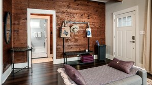 Una habitación con pared de madera, una cama con ropa de cama estampada, una mesita pequeña y una puerta.