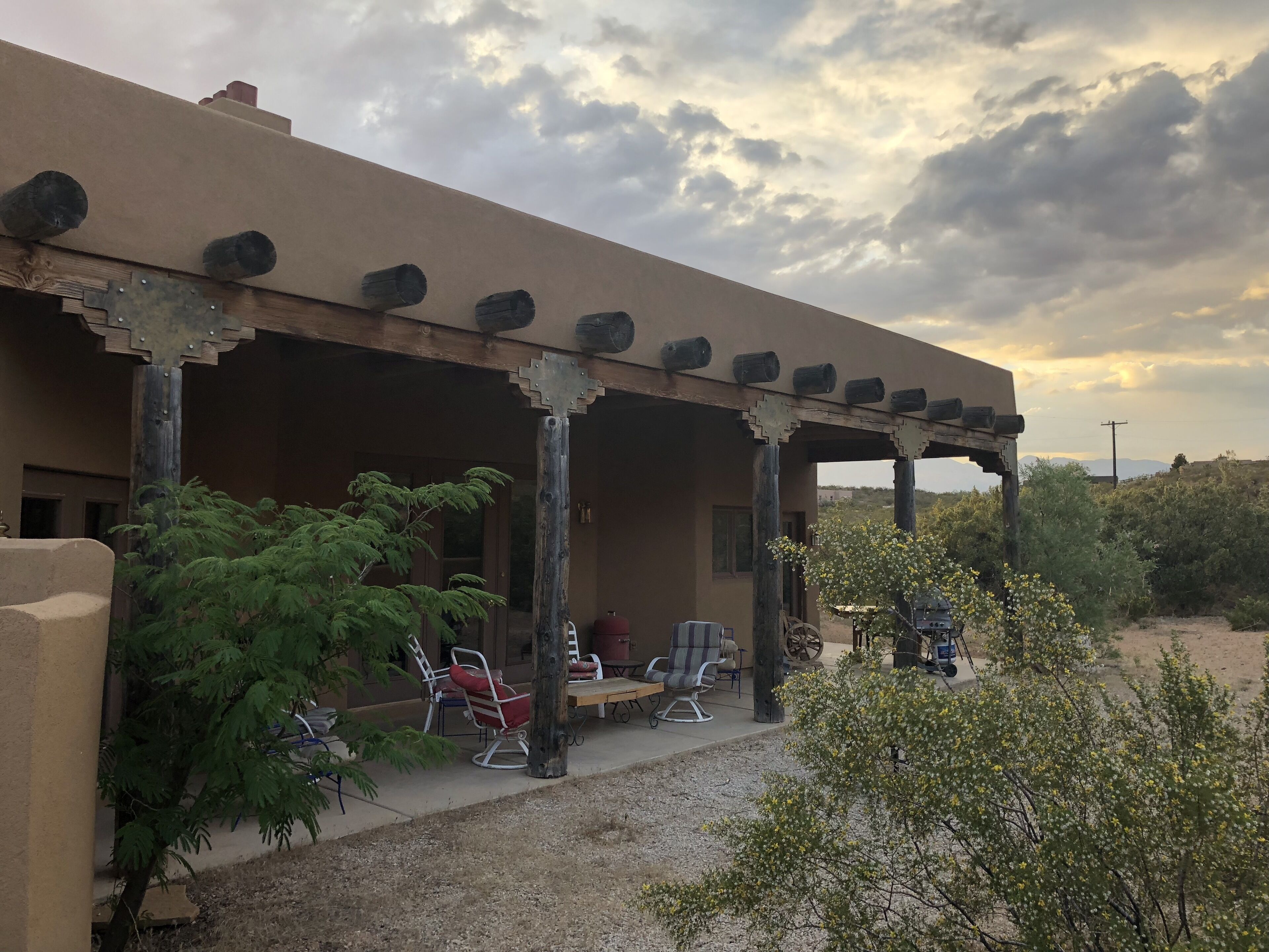A covered outdoor seating area with chairs and tables, surrounded by desert vegetation.