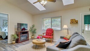 A living room with a TV, a fireplace, a red chair, a grey sofa, and a ceiling fan. - Mom's Place in Jemez - 1 Mi to Hot Spring (Jemez Springs)
