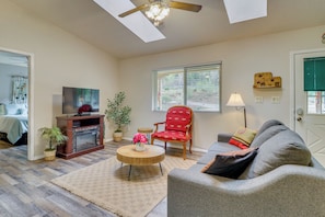 A living room with a TV, a fireplace, a red chair, a grey sofa, and a ceiling fan.
