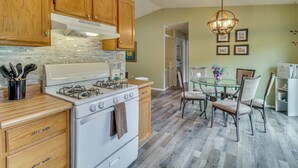 A kitchen with wooden cabinets, a white stove, and a dining area with a glass table and chairs. - Mom's Place in Jemez - 1 Mi to Hot Spring (Jemez Springs)