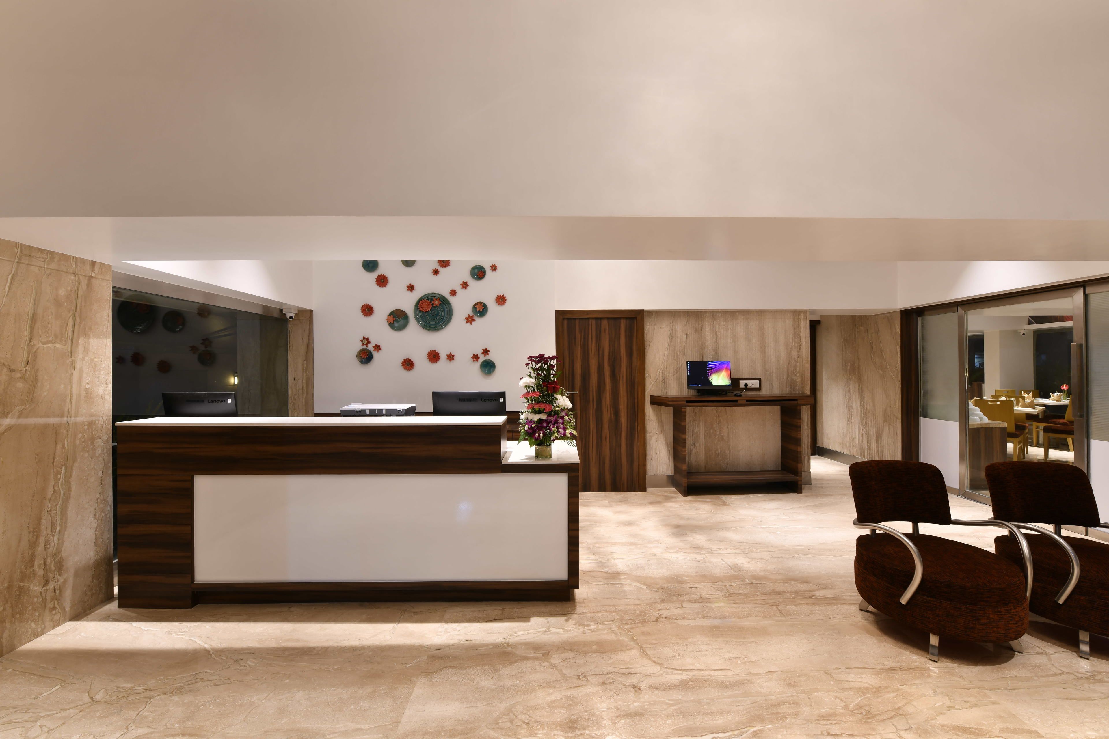 A modern reception area with a marble floor, wooden reception desk, and a wall decorated with circular patterns. There are two chairs and a small table with a vase of flowers.
