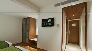 Habitación de hotel con dos camas, un armario de madera, un televisor en la pared y una puerta que da a otra habitación.