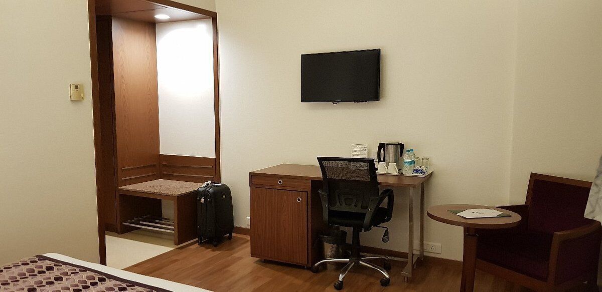 A hotel room with a wooden desk, a chair, a television, and a small table with a chair.