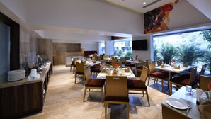 Un comedor moderno con varias mesas y sillas, una estación de buffet y grandes ventanales con vistas al exterior.