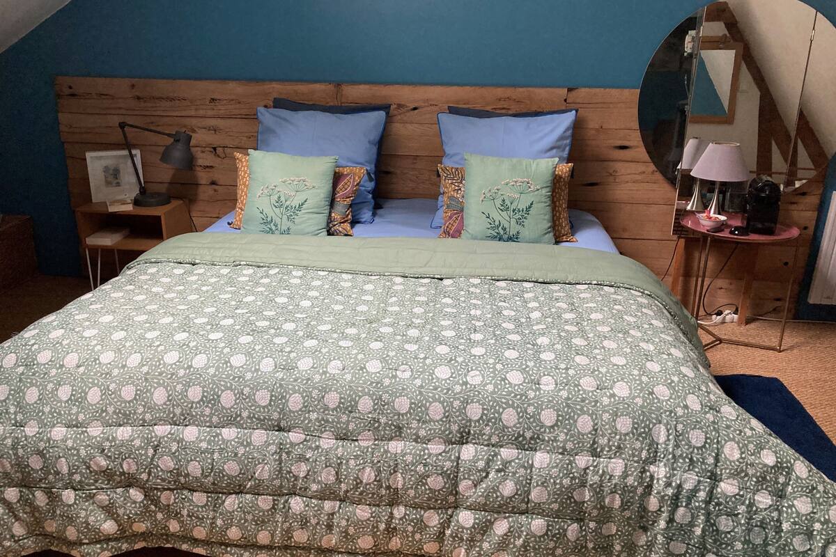 A bedroom with a wooden headboard, a green patterned bedspread, and multiple pillows.