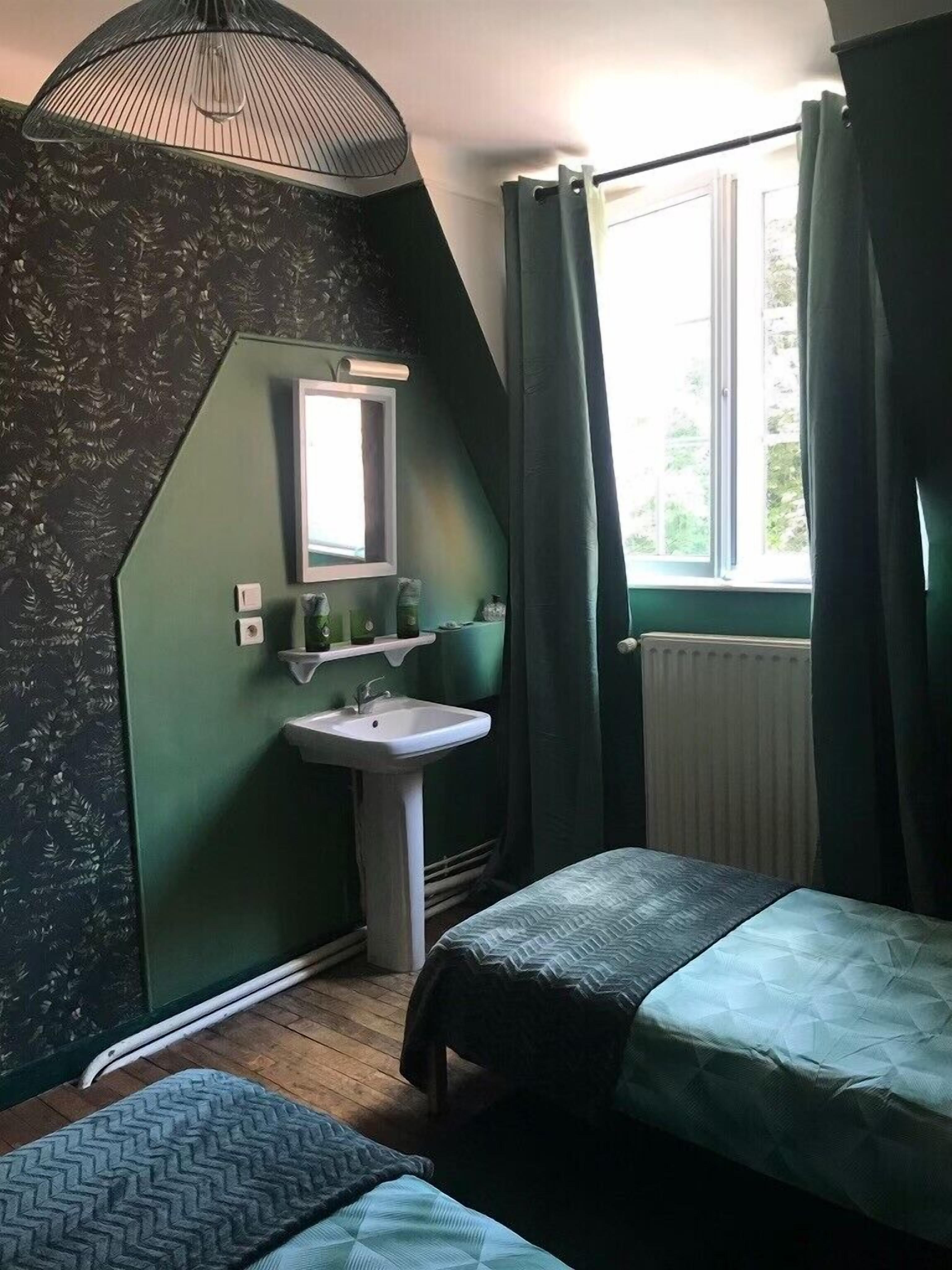 A room with a green wall, a window with curtains, a sink, and two beds.