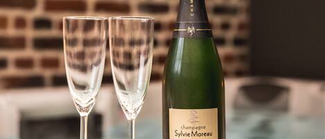 A bottle of champagne and two glasses on a white surface with a brick wall in the background.
