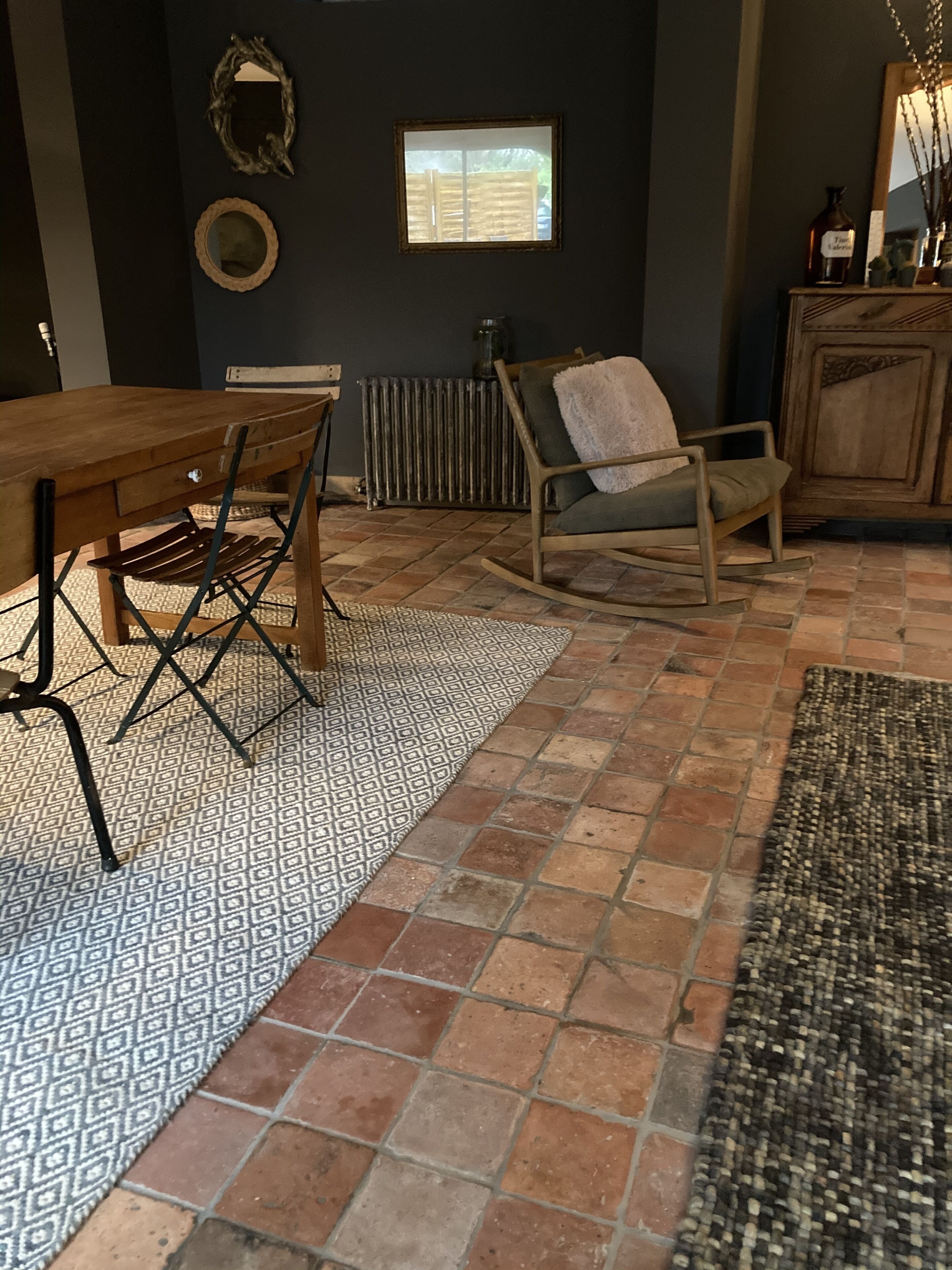 Une pièce avec une table à manger en bois, un fauteuil à bascule, un tapis à motifs et un radiateur.