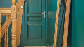 A room with a wooden staircase, a teal door, and a large mirror leaning against the wall.