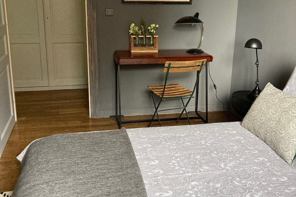 A bedroom with a bed, a desk, a chair, a lamp, and a framed picture on the wall.